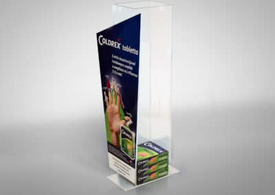Toronyszerű Coldrex asztali terméktartó display az elején szabálytalan négyszög alakú felülettel, amin a cég logója valamint a termék képe és kreatívja látható. Mögötte a plexi tárolórészben Coldrex tabletták dobozai sorakoznak egymásra fektetve.