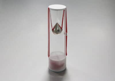 Egyedi díjtartó plexihenger aminek a közepén csepp alakú fém díj lóg vörös szallagon.
